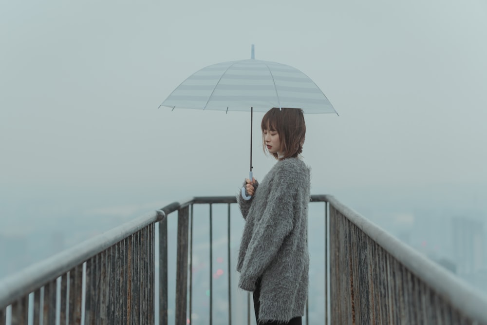 woman in gray coat holding umbrella standing on bridge during daytime