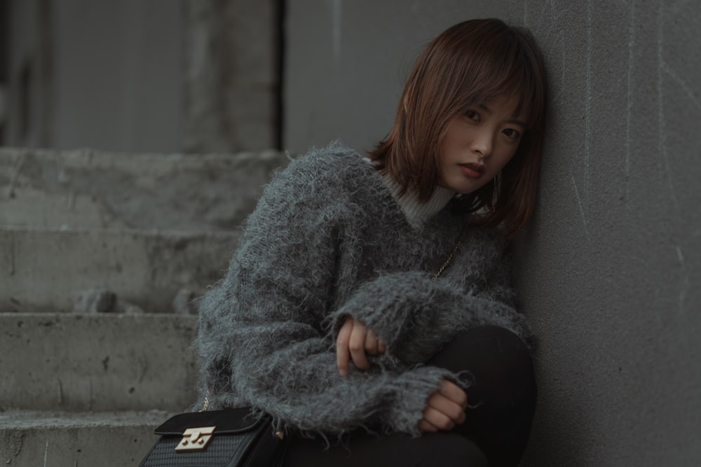 woman in gray sweater and black pants sitting on gray concrete bench