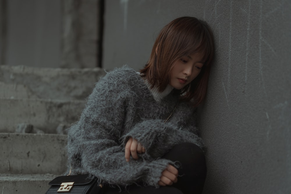 woman in gray sweater sitting on gray concrete bench