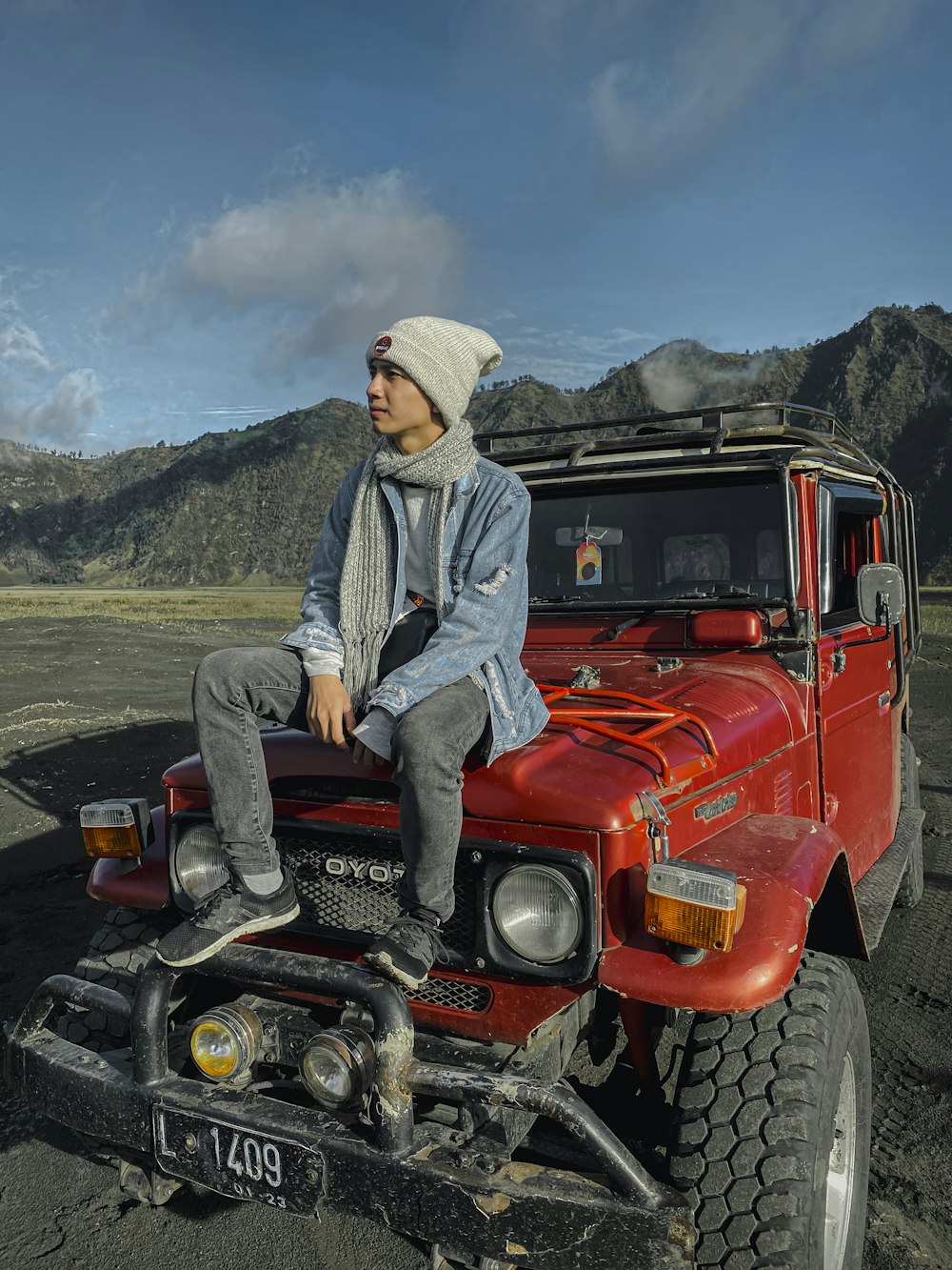 man in gray hoodie sitting on red jeep wrangler