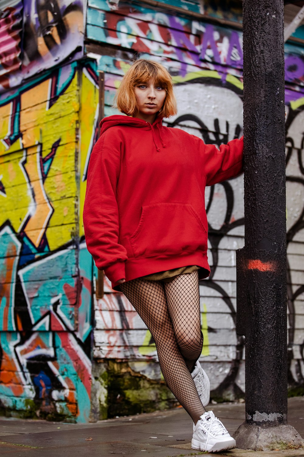 woman in red hoodie and black skirt leaning on black metal fence