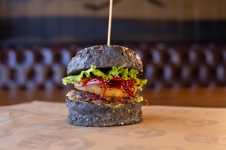 A gourmet burger with a black sesame seed bun, topped with lettuce, a slice of grilled pineapple, a beef patty, and a generous amount of sauce.