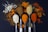 A dark background with five spoons of various spices arranged in a row. The different spices include a white powder, a brown powder, a yellow powder, an orange powder, and a red powder. Some spices are scattered around the spoons, creating a colorful and textured presentation.