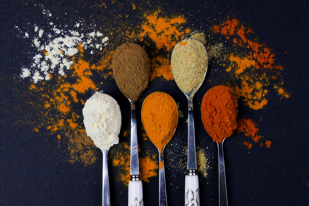 brown powder on silver spoon, Colorful various herbs and spices for cooking on dark background