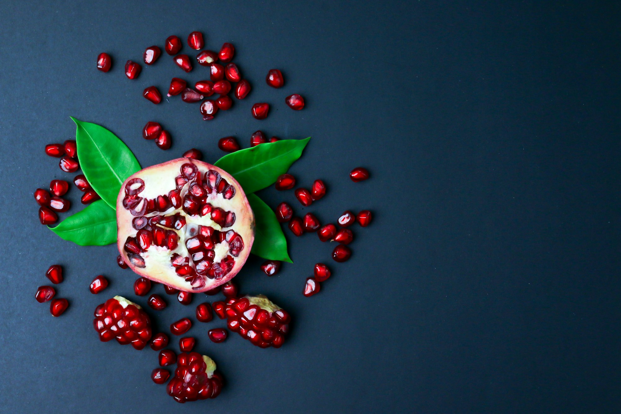 Fresh pomegranate with green leaves isolated on black background