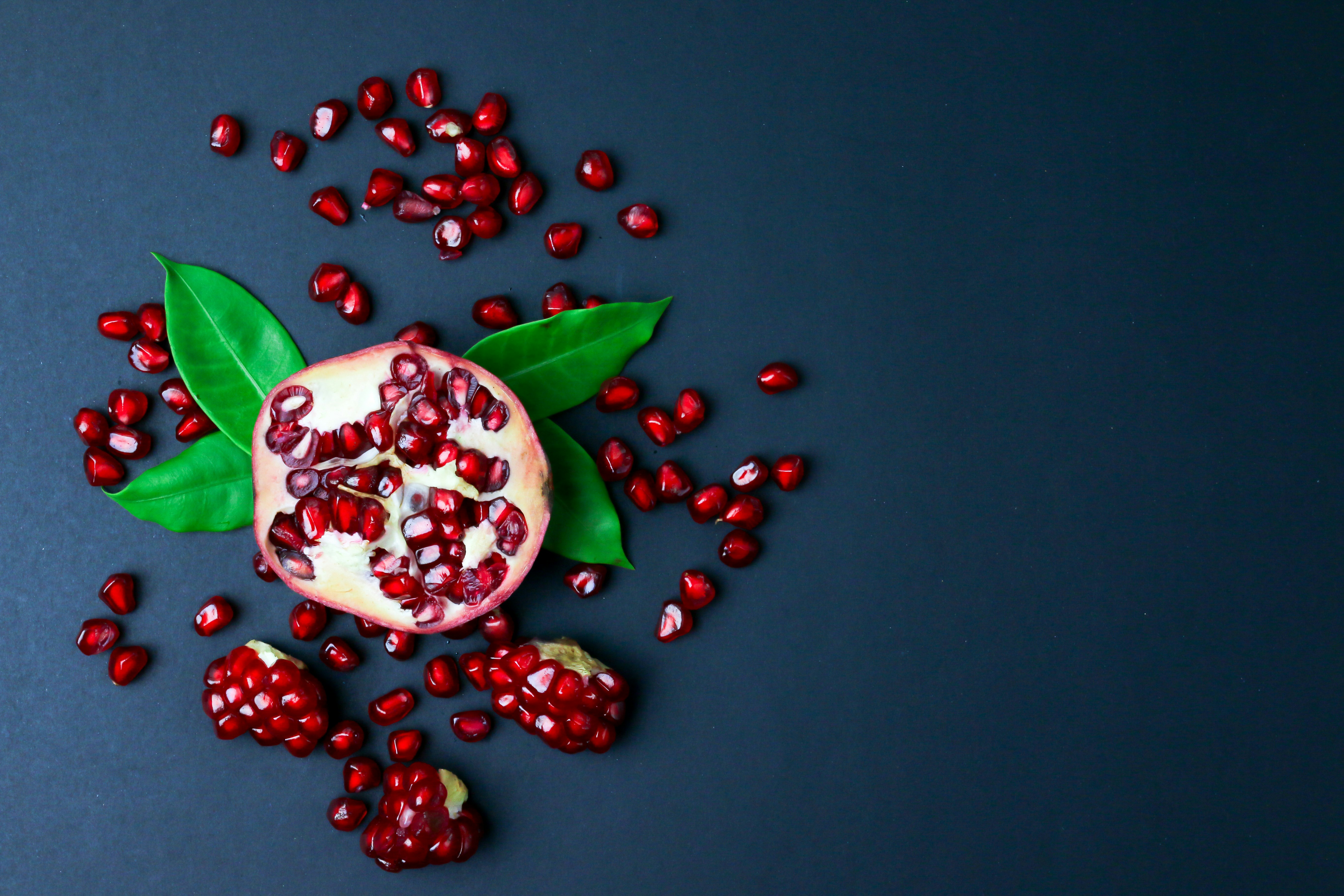 great photo recipe,how to photograph fresh pomegranate with green leaves isolated on black background; red and white round fruits on black surface