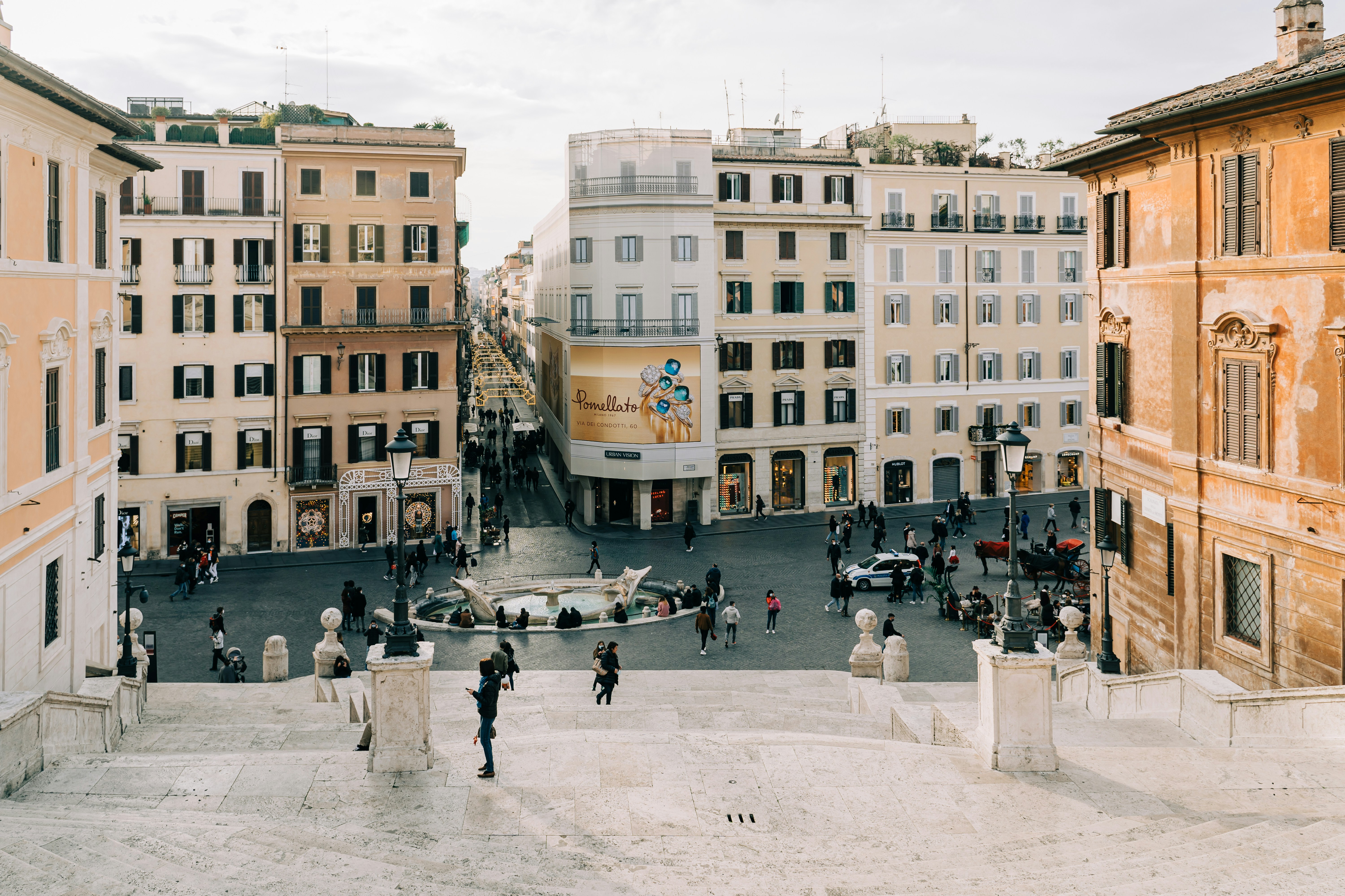 People walking along the street surrounded by tall buildings at Piazza di Spagna, a place in Rome where several Roman festivals take place.