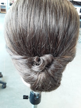 A neatly styled updo showcasing brown hair twisted into a bun. The hair appears smooth and well-groomed with a shiny texture. The background is slightly blurred, focusing attention on the hairstyle.