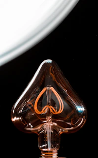 An artistic shot of a bulb filament shaped like a heart glowing softly.