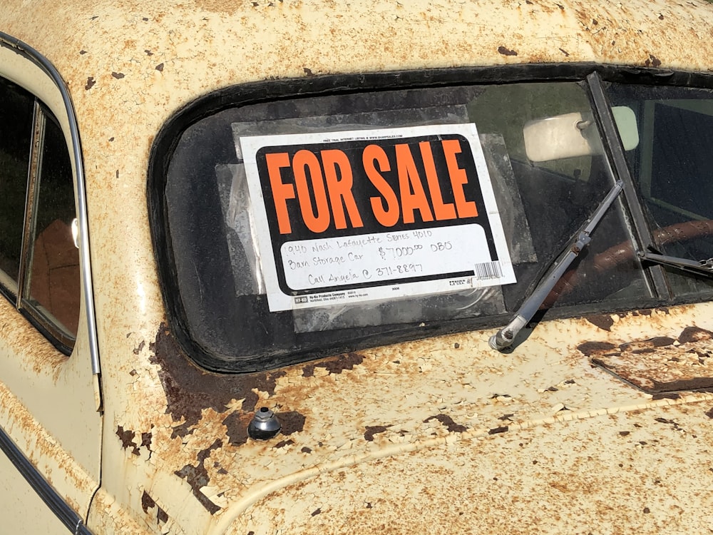 a rusted out car with a for sale sign on it