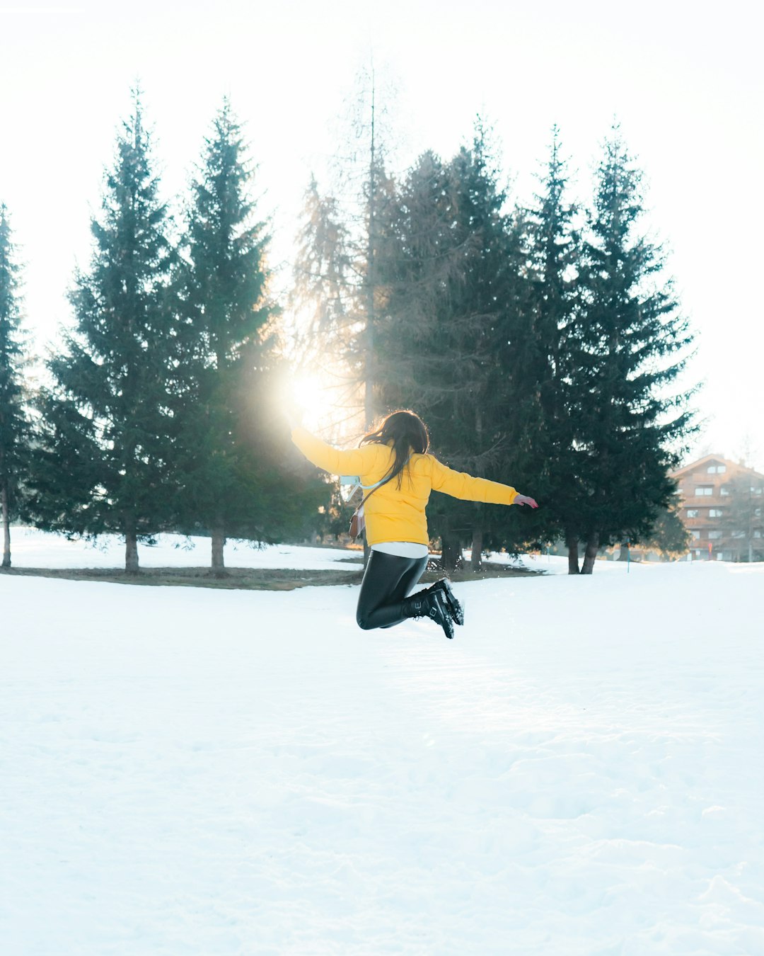 woman in yellow jacket and black pants jumping on snow covered ground during daytime