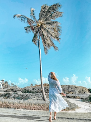woman in white dress standing near palm tree during daytime