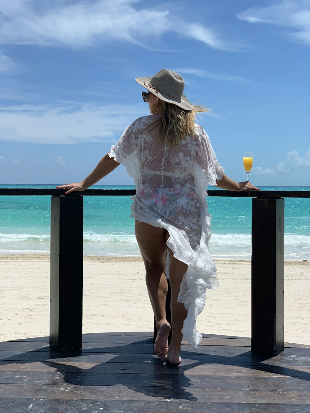 Mujer con camisa floral blanca y rosa y sombrero marrón de pie en la playa durante el día