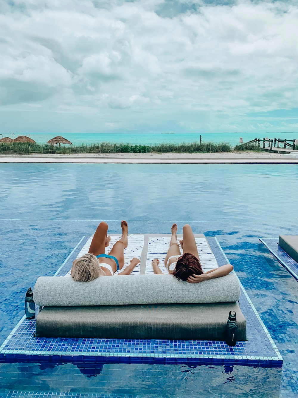 2 women lying on blue towel on blue swimming pool during daytime
