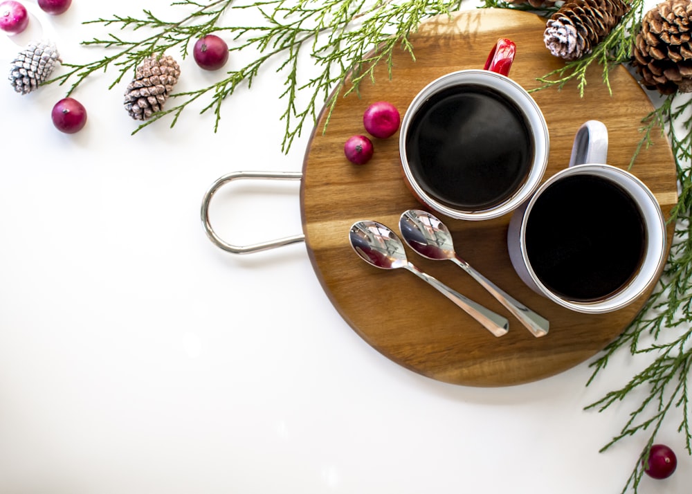 two cups of coffee on a wooden tray with spoons