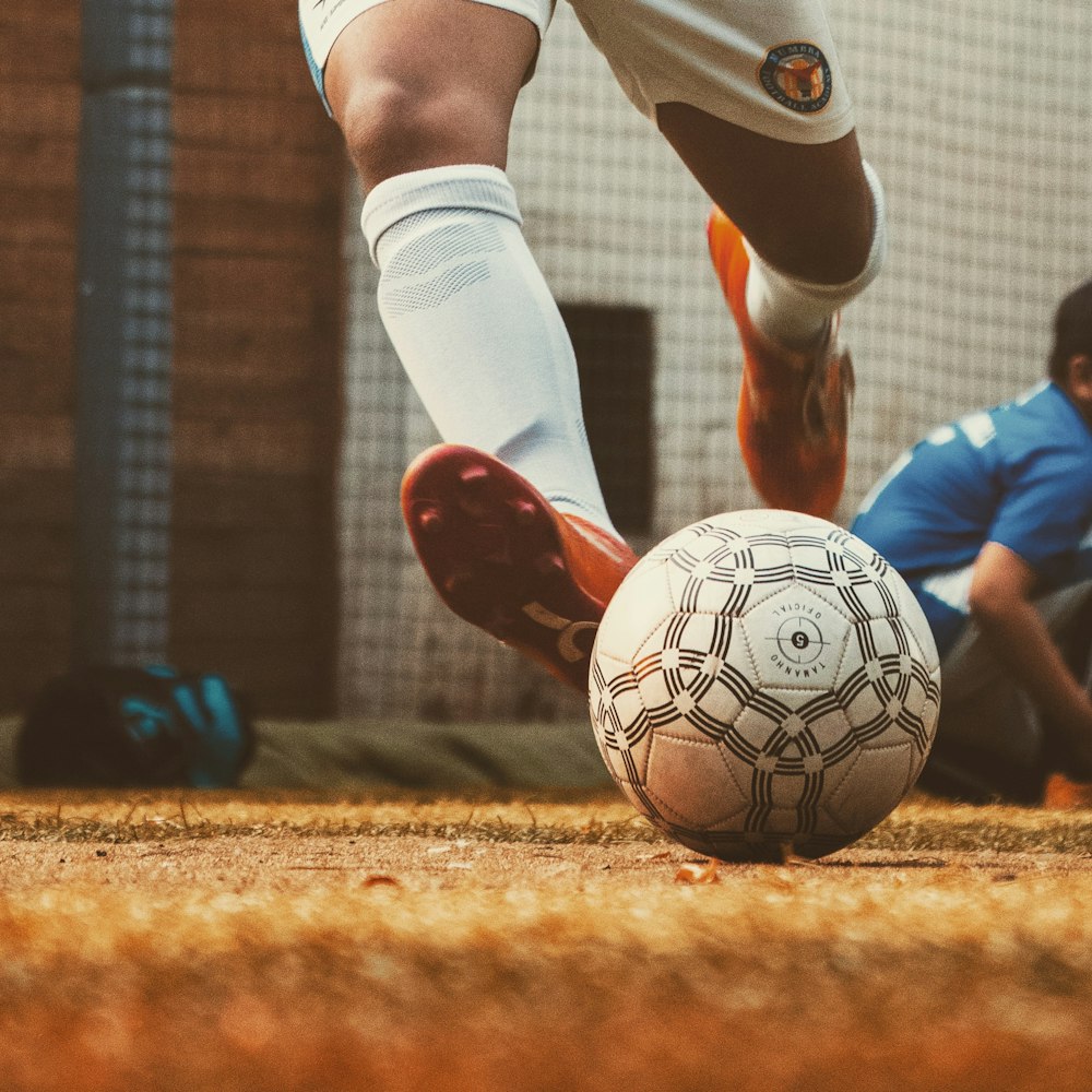 personne en maillot de football blanc et rouge donnant un coup de pied dans le ballon de football