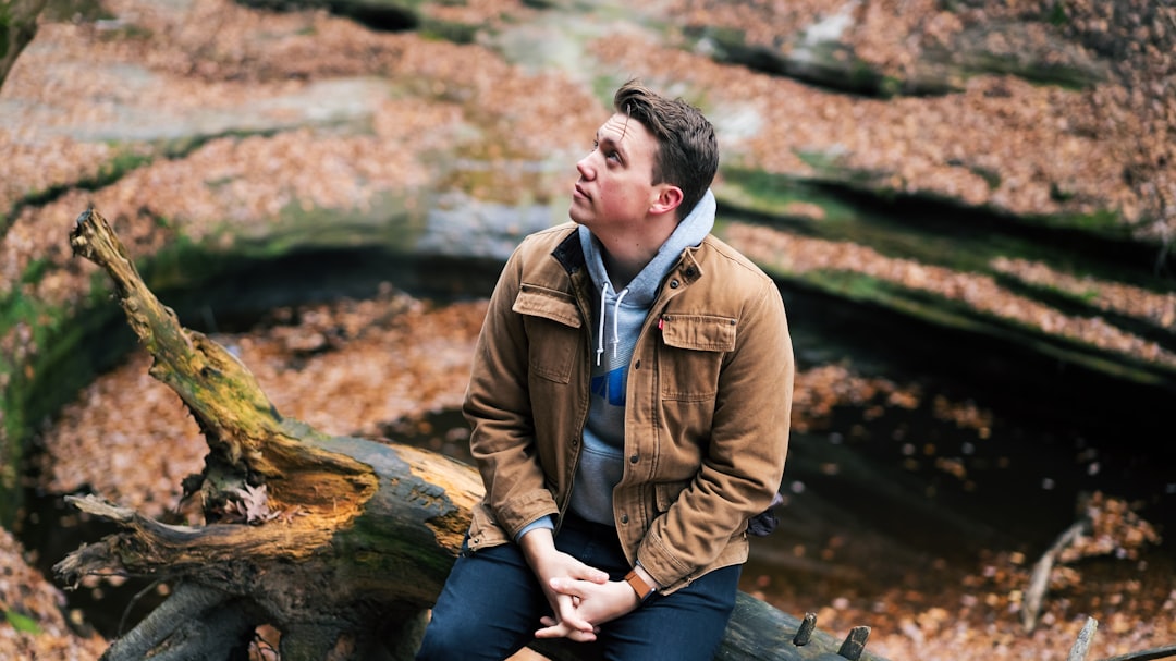 man in brown jacket sitting on brown rock during daytime