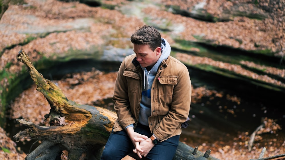 man in brown jacket sitting on brown tree log during daytime