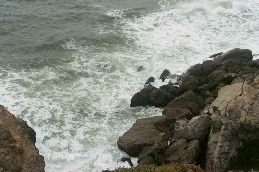 brown rocky shore with ocean waves crashing on rocks during daytime