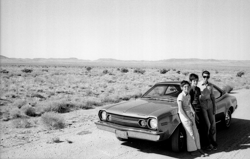 man and woman standing beside car in grayscale photography