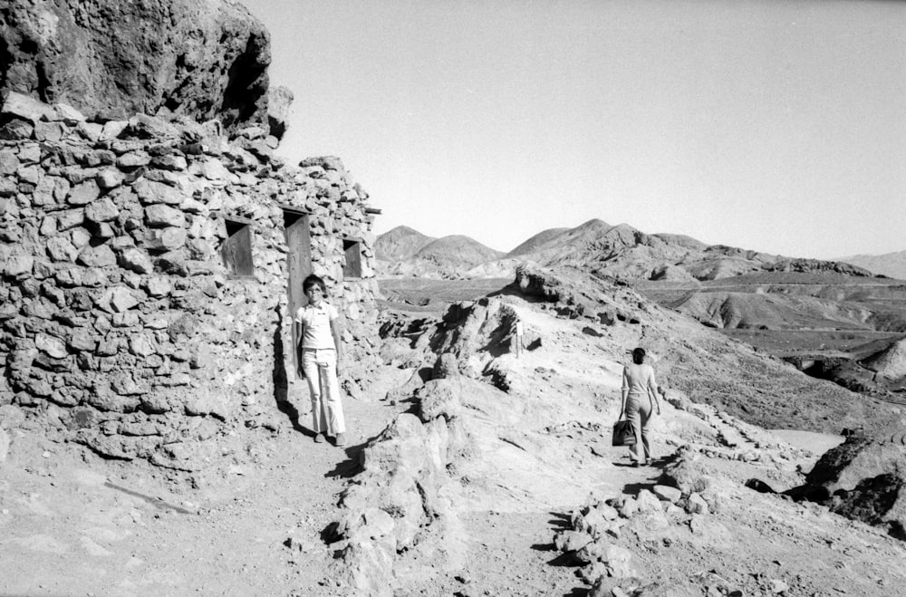 grayscale photo of man and woman standing on rock formation