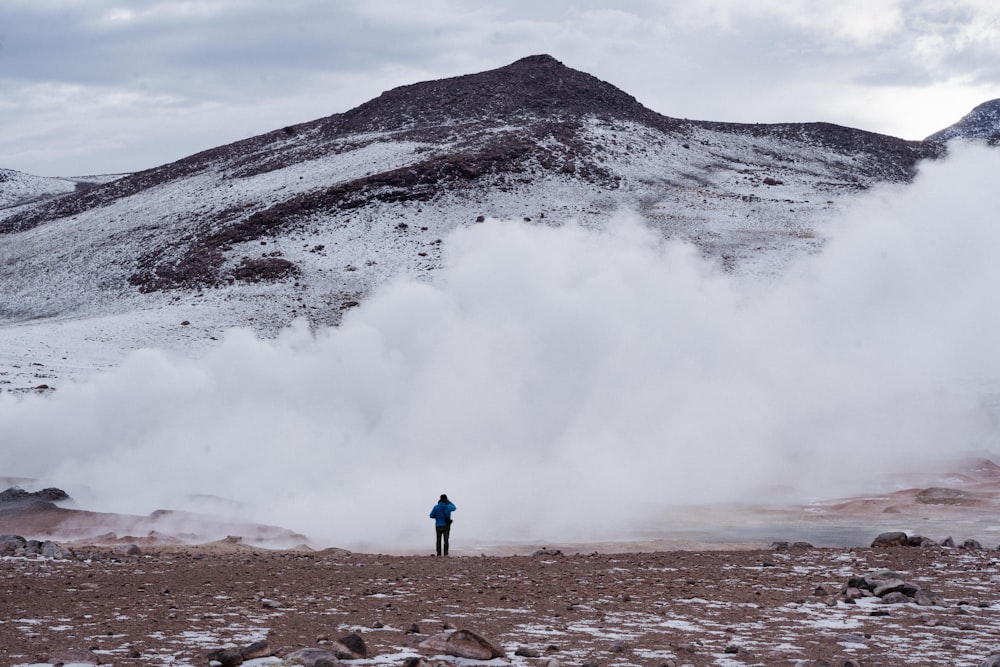 person in blue jacket standing on brown soil near white snow covered mountain during daytime