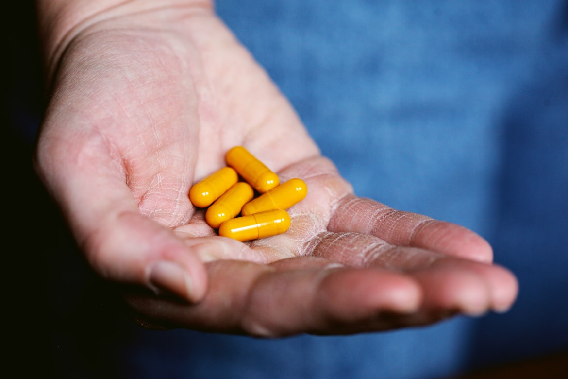 Person holding orange colored capsules in hand.