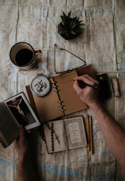 A notebook open with a handwritten budget plan, surrounded by coins and a small cross pendant.