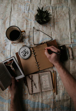 A notebook open with a handwritten budget plan, surrounded by coins and a small cross pendant.