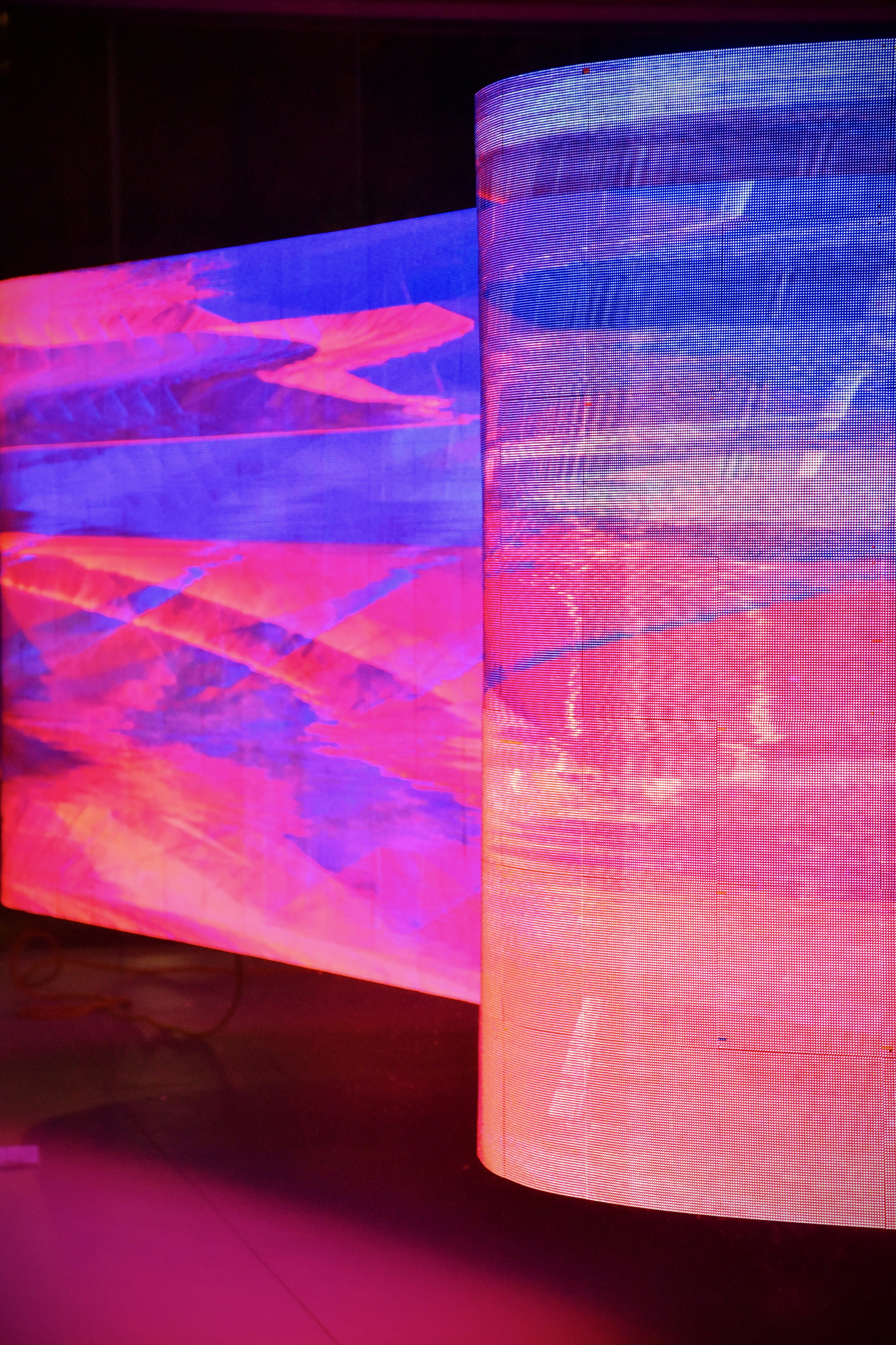 Two large curved LED screens display vibrant abstract digital patterns.