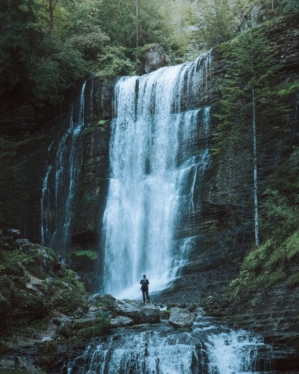 persona in piedi sulla roccia vicino alle cascate durante il giorno