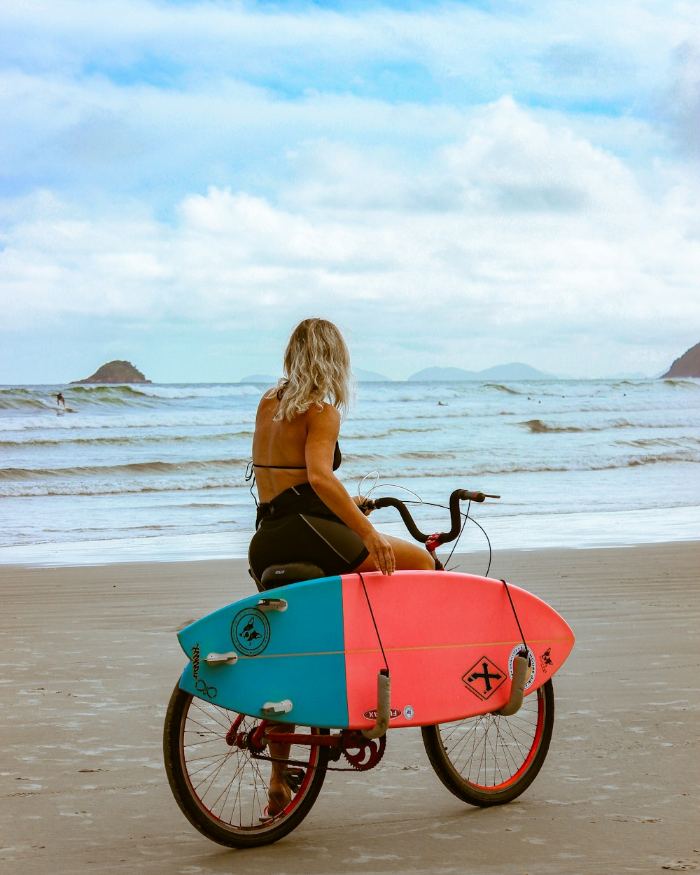Mujer en camiseta sin mangas negra montando en bicicleta roja y azul en la playa durante el día