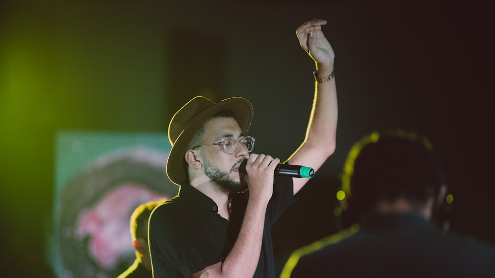 Un hombre con sombrero y gafas cantando en un micrófono