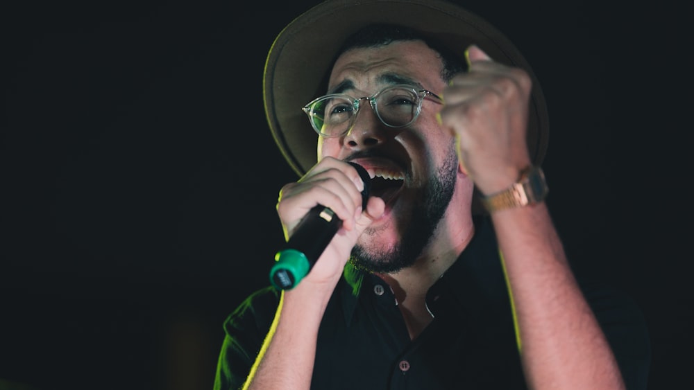 a man with a hat and glasses singing into a microphone