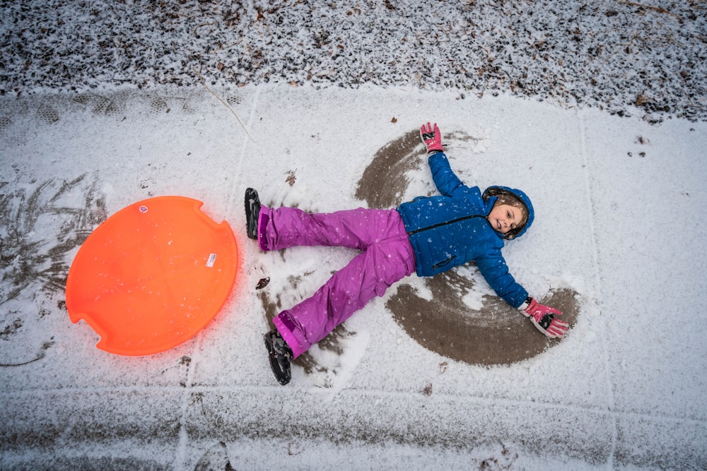 boy in blue and red long sleeve shirt and pink pants holding orange round plastic