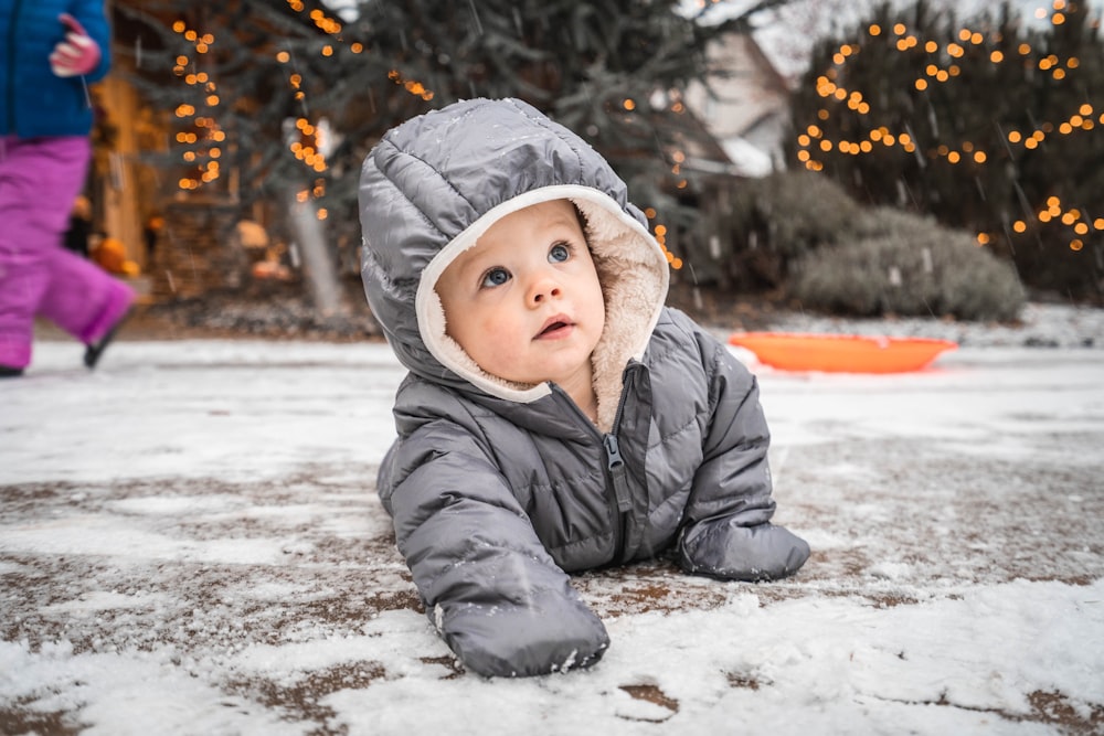 雪に覆われた地面に横たわる灰色の冬用ジャケットを着た子供