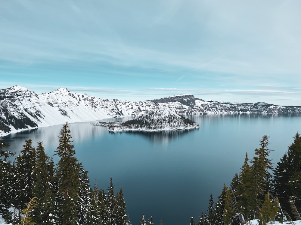 lake surrounded by snow covered mountains and trees under blue sky during daytime