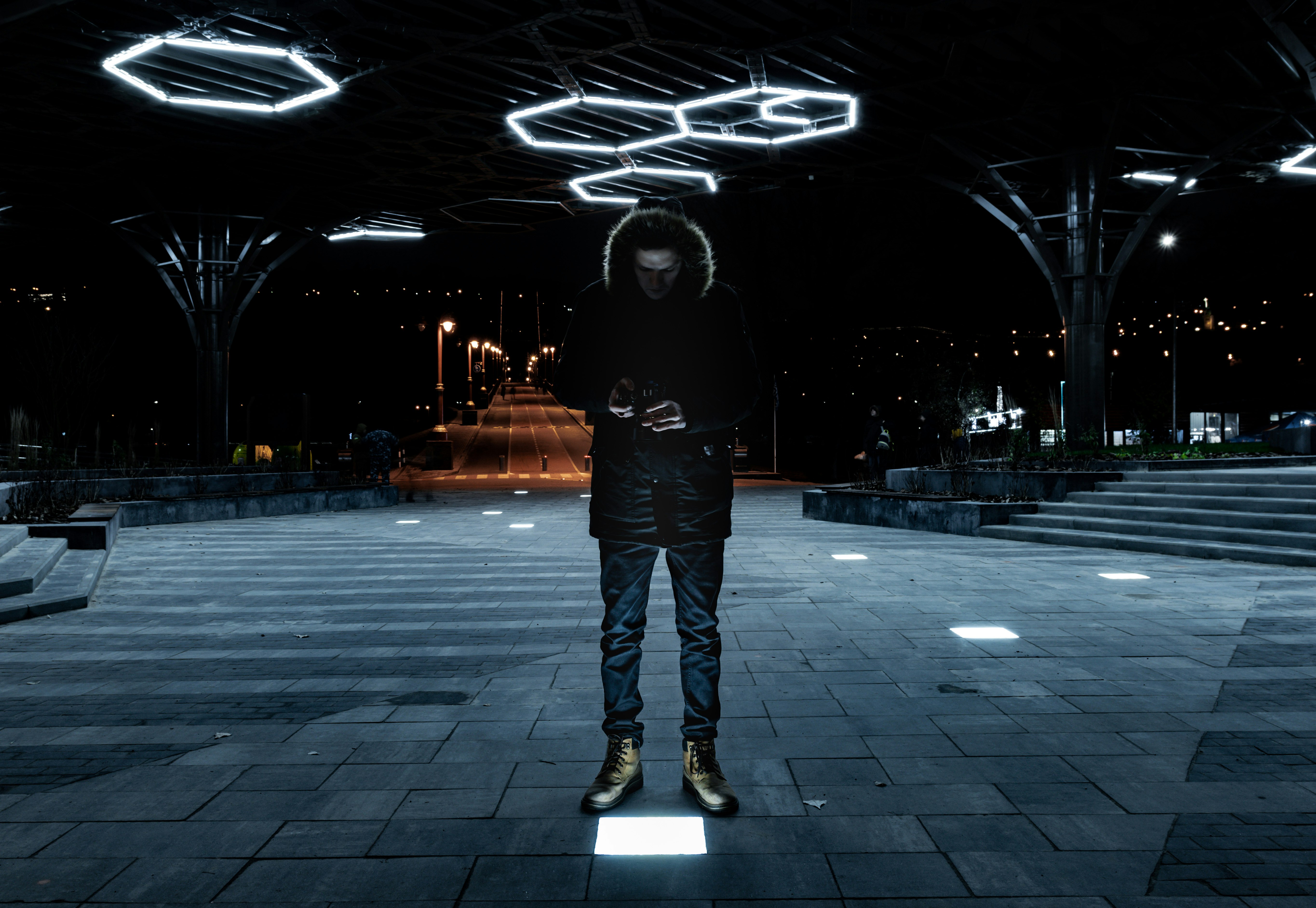 man in black and white hoodie standing on gray concrete pavement during night time