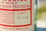 A close-up of a bottle label with text in red and black on a light background. The label includes wording related to Mexico and has a lot number handwritten as 16/7160.