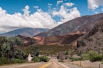 gray asphalt road near brown mountains under blue and white sunny cloudy sky during daytime