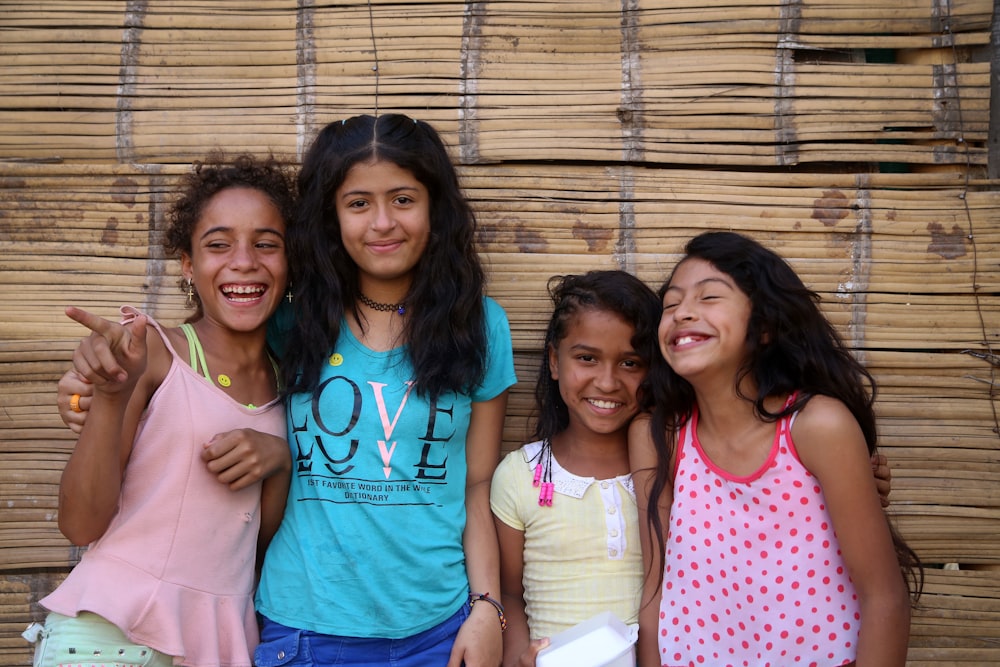 3 women smiling and standing beside brown wall