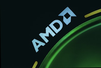 A dark background with the word 'AMD' in bold, white text accompanied by the distinctive AMD logo, partially visible on the right side. The logo is set against a green, circular shape with a smooth gradient, creating a sleek and modern appearance.