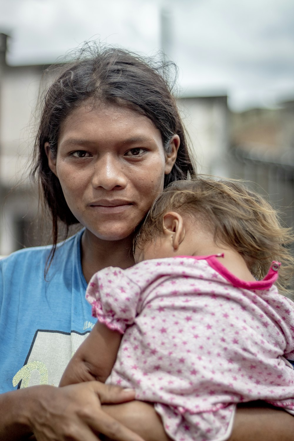 Mujer en camisa azul de cuello redondo que lleva a la niña en camisa floral rosa y blanca