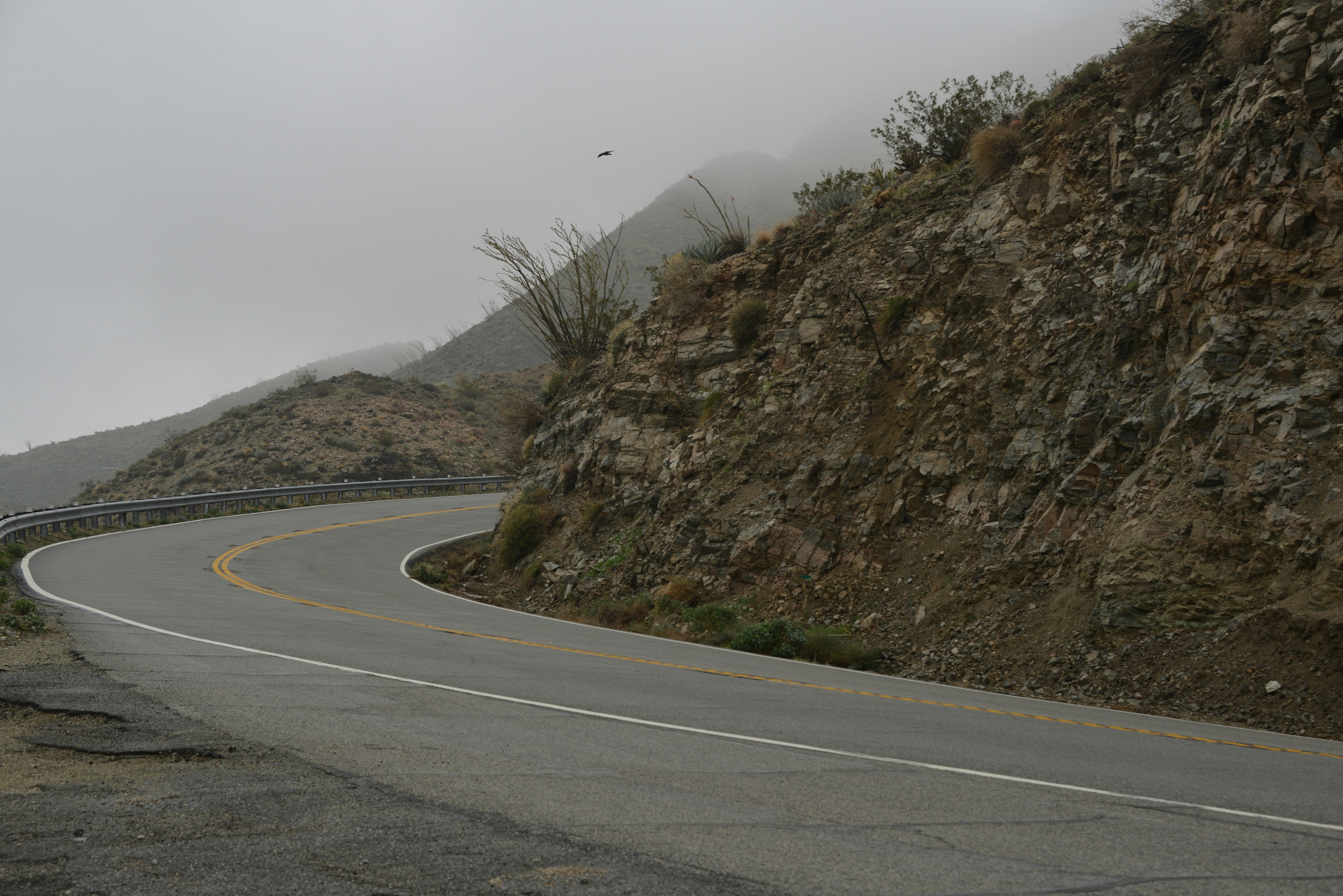 gray asphalt road beside brown rocky mountain during daytime