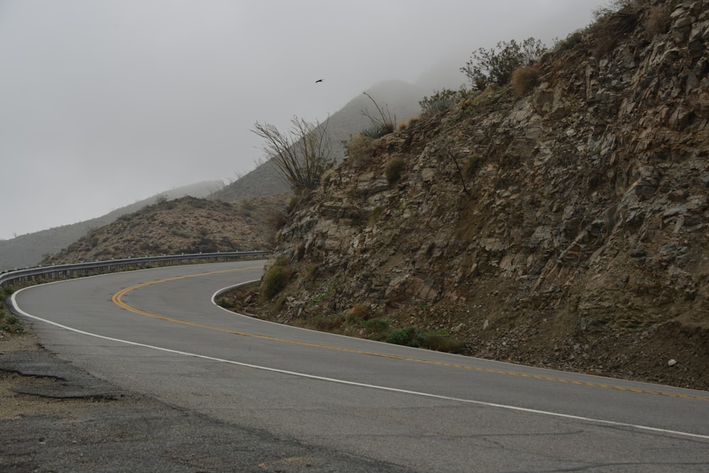 strada asfaltata grigia accanto alla montagna rocciosa marrone durante il giorno