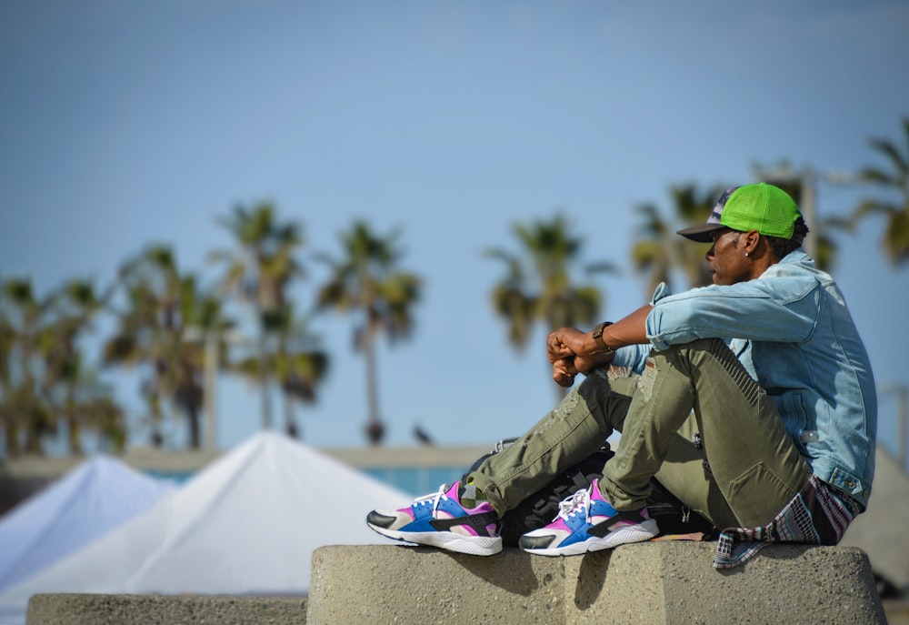 man in green jacket and green cap sitting on white concrete bench during daytime
