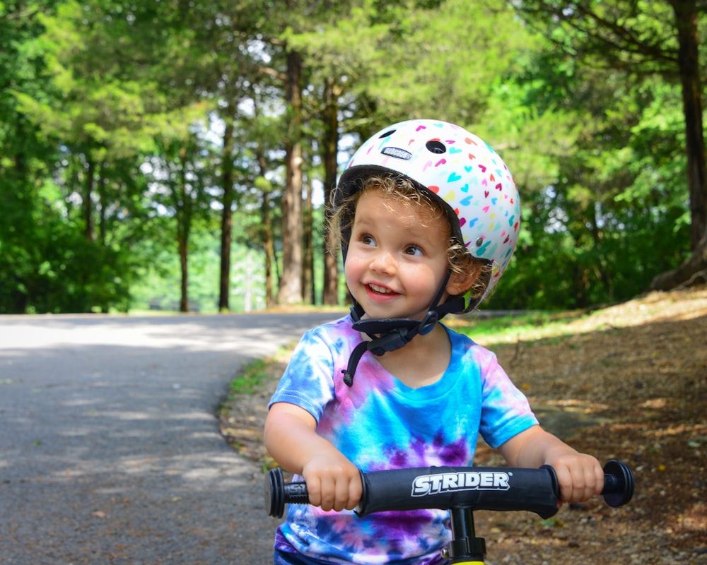 ピンクと白のヘルメットをかぶった女の子が昼間、道路で自転車に乗っている