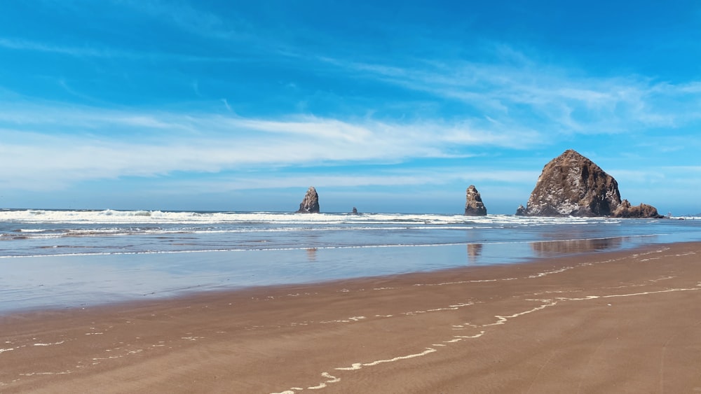 brown sand beach with rocks on the side under blue sky during daytime