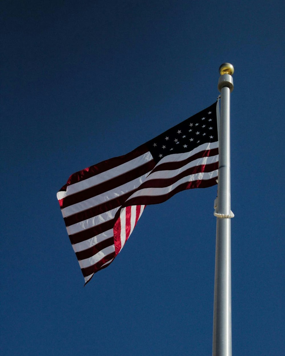 日中の白いポールに旗を立てる米国