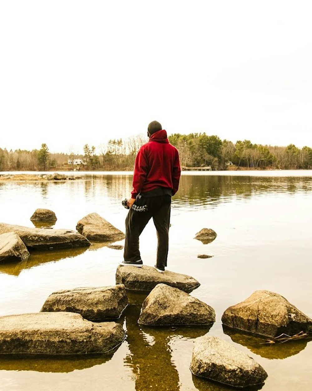 man in red hoodie standing on rock near body of water during daytime